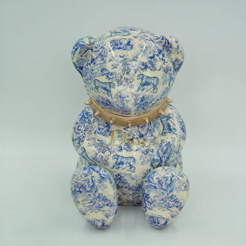A ceramic bear figurine with a blue and white pattern featuring animals and nature scenes. The bear wears a gold collar with spikes, and the word 