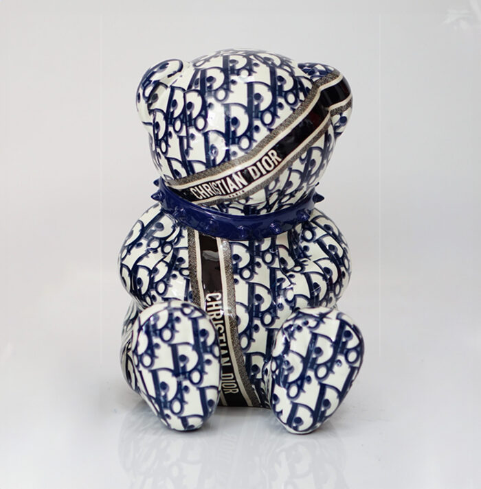 A ceramic bear figurine with a blue and white pattern, featuring the text "CHRISTIAN DIOR" on ribbons wrapped around it.