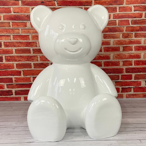 Glossy white teddy bear sculpture in front of a red brick wall.