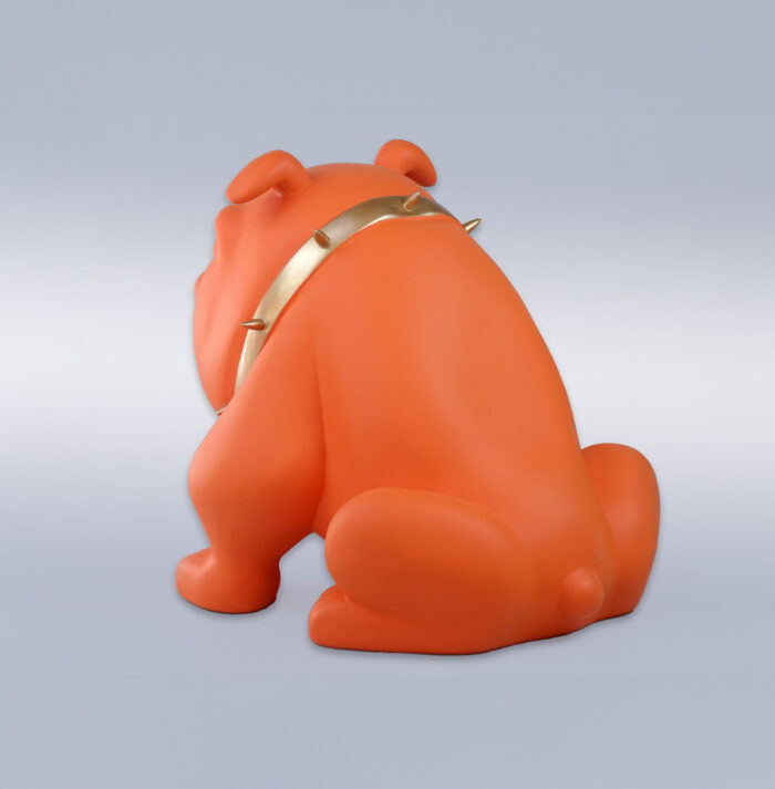 Orange bulldog sculpture with a gold spiked collar, facing away from the viewer, against a plain background.