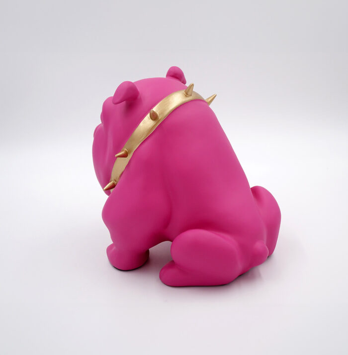 Pink bulldog figurine with a gold spiked collar facing away.