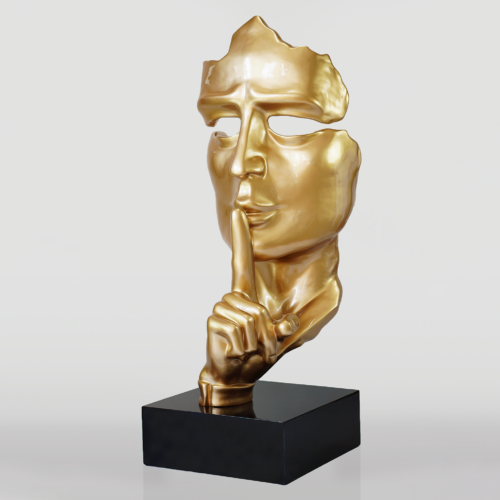 Golden sculpture of a face with a hand gesturing for silence, placed on a black base.