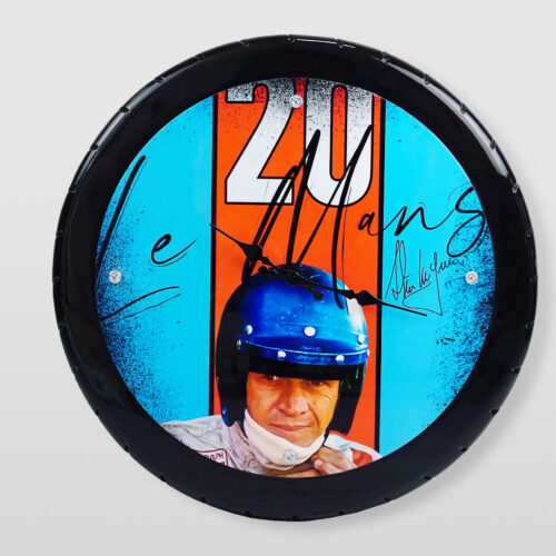 Zegar ścienny z motywem Le Mans, przedstawiający mężczyznę w kasku wyścigowym na tle niebiesko-pomarańczowym.