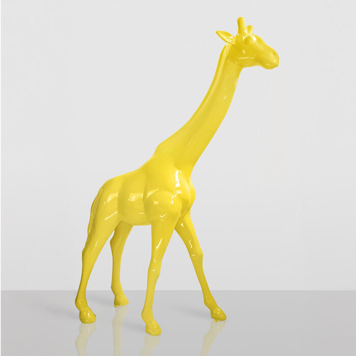 Glossy yellow giraffe sculpture standing on a reflective surface against a plain light gray background.