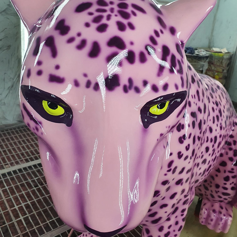 Close-up of a pink leopard sculpture with black spots and yellow eyes.