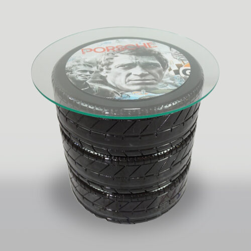 A table made from stacked tires with a glass top, featuring a vintage Porsche-themed image under the glass.