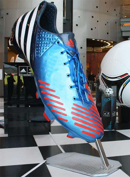 A large Adidas football boot displayed on a stand inside a building.