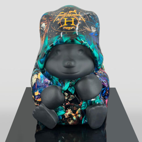 Sculpture of a bear-like figure with a black matte finish, wearing a colorful coat adorned with butterfly and foliage patterns and an emblem featuring an