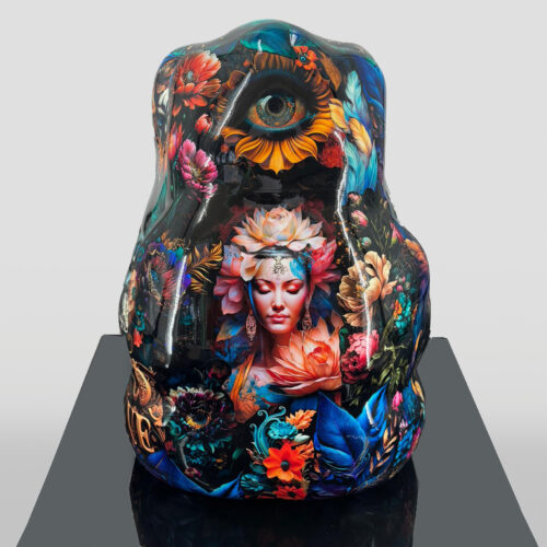 A vibrant sculpture decorated with a detailed, multicolored floral design, featuring a large eye and a serene woman's face with a flower headdress in the center.