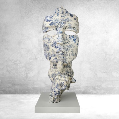 Decorative sculpture shaped as a face with a finger in front, featuring intricate blue and white pastoral scenes, mounted on a rectangular base.