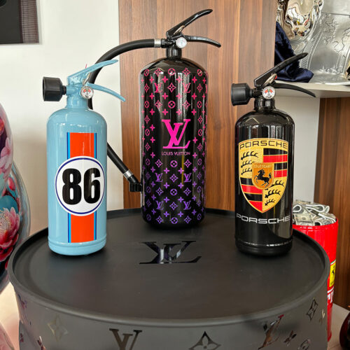 Three designer fire extinguishers on display: left is light blue with the number