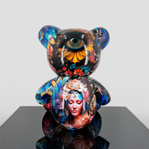 A colorful teddy bear sculpture with an artistic design featuring a large eye on its head and a serene woman's face surrounded by flowers and feathers on its body.
