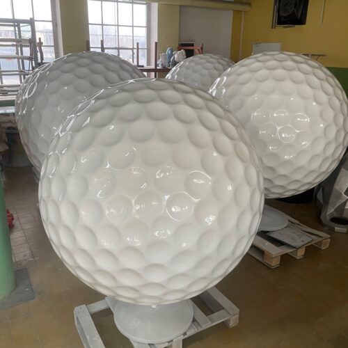 Large white spherical objects resembling oversized golf balls, positioned indoors on pallets.