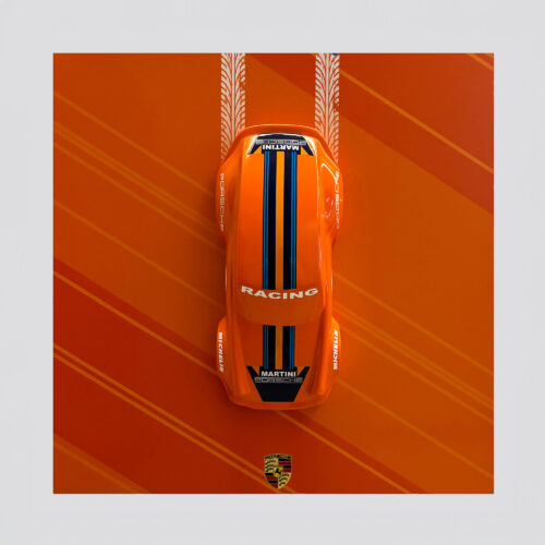 Top view of an orange Porsche race car with blue racing stripes on an orange background with tire marks and a Porsche logo.