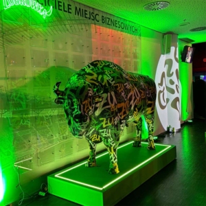 Sculpture of a bison with inscriptions, illuminated by green light, standing on a lit pedestal in a room.