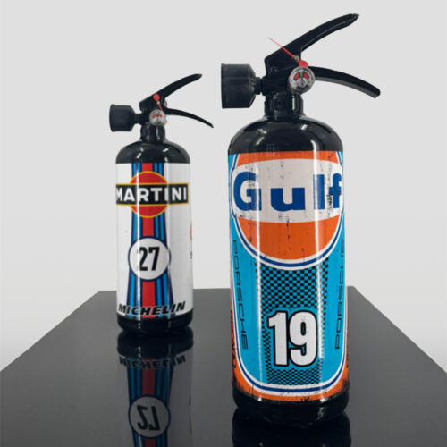 Two fire extinguishers decorated as vintage racing fuel cans with Gulf and Martini logos standing on a reflective black surface.