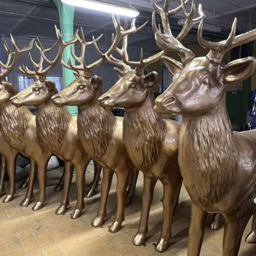 Row of golden deer statues with antlers positioned indoors on a tiled floor.