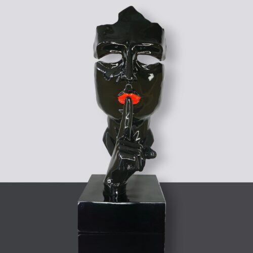 Black sculpture of a mask with orange lips and a hand in front, making a shushing gesture, on a rectangular black base.