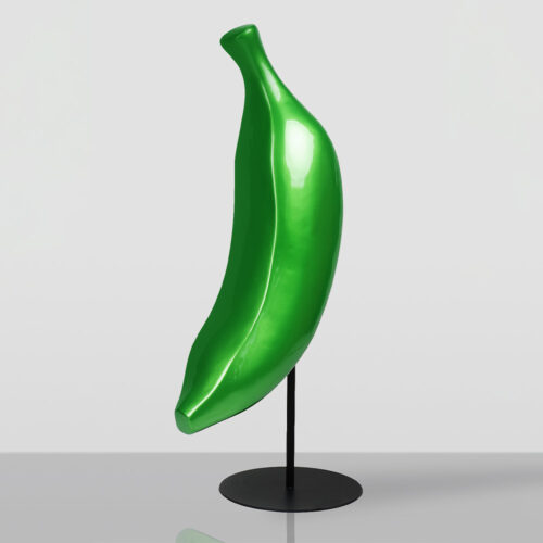 Glossy green banana-shaped sculpture mounted on a black metal stand with a round base on a gray reflective surface against a light gray background.