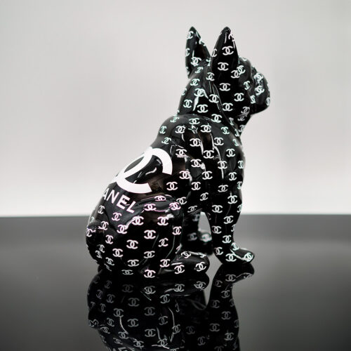 Black dog figurine covered with Chanel logos, sitting on a reflective black surface.