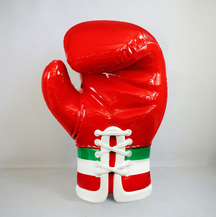 Red boxing glove with white laces and green and white stripes on the cuff against a plain background.