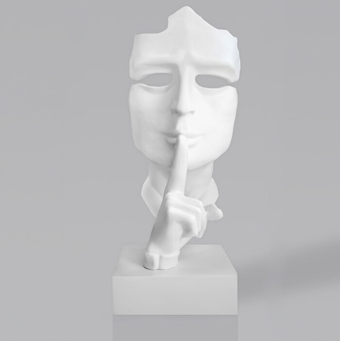 White statue of a fragmented face with a finger gesture indicating silence on a rectangular base.