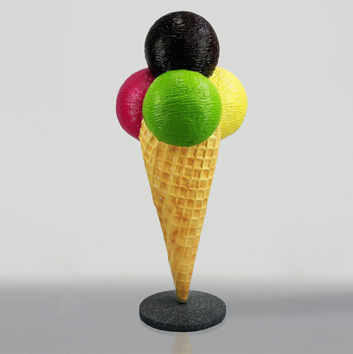 Plastic model of an ice cream cone with four scoops, in black, red, green, and yellow, displayed on a round black stand.