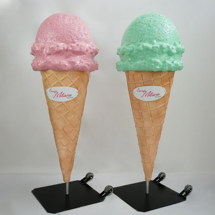 Two large ice cream cone sculptures with pink and green ice cream on top, mounted on stands with wheels.