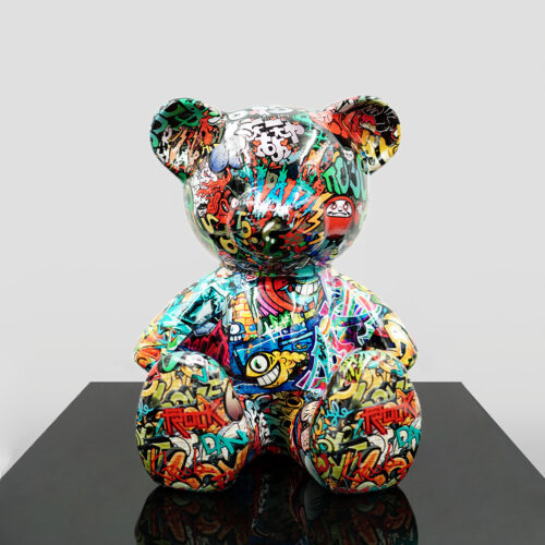 Graffiti-covered bear sculpture on a reflective black surface.