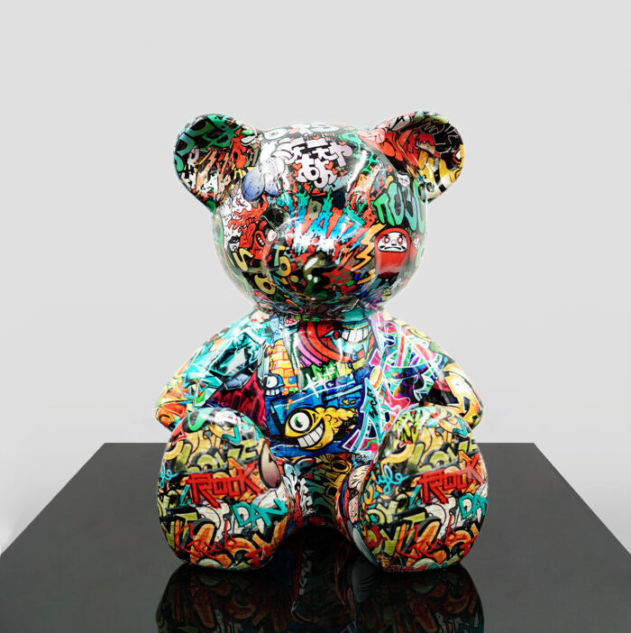 Graffiti-covered bear sculpture on a reflective black surface.