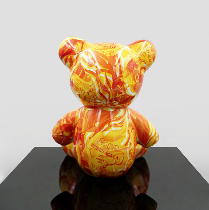 A colorful bear-shaped sculpture with an orange and yellow swirling pattern sits on a black reflective surface.