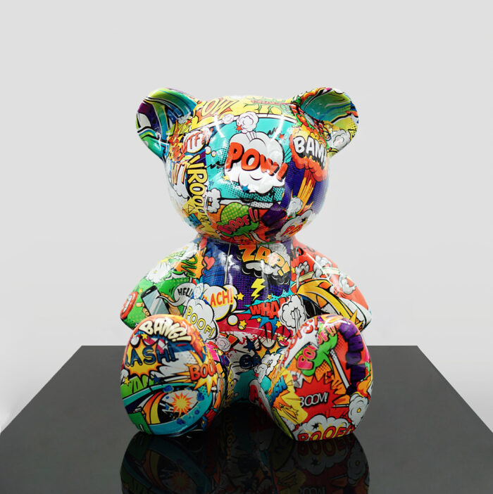 A multicolored teddy bear statue covered in comic book-style illustrations, featuring onomatopoeic words like "POW," "BAM," and "ZAP."