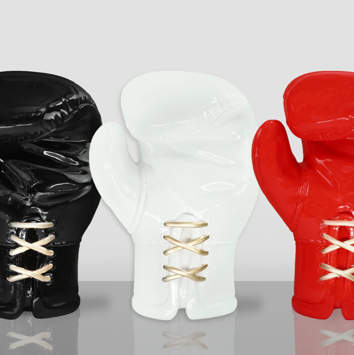 Three ceramic sculptures of boxing gloves in black, white, and red, each with gold laces, displayed against a light gray background.