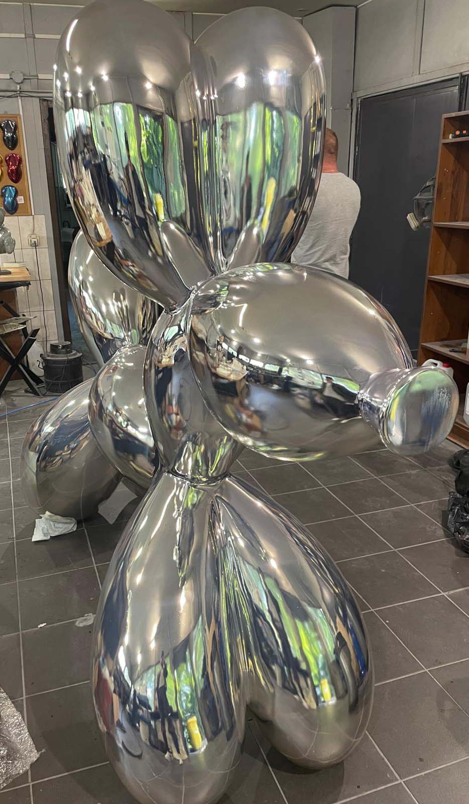 Balloon Dog Sculpture by 3Dform 1 Srebrna rzeźba przypominająca balonowego psa w pracowni artystycznej.