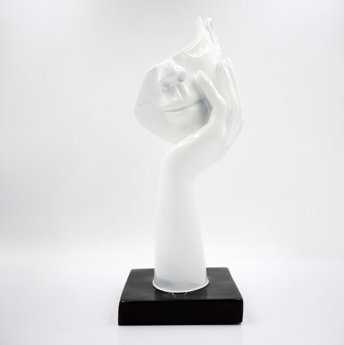 White abstract ceramic sculpture of a face with a hand resting on a black square base.