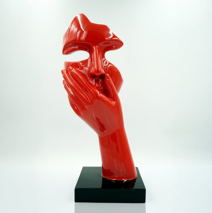 Red abstract sculpture depicting a face and a hand covering its mouth, on a black base.