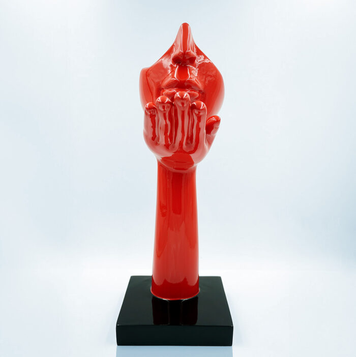 Red sculpture of a hand with an abstract face, mounted on a black square base.