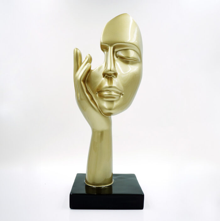 Abstract golden face sculpture with an elongated finger touching the cheek, mounted on a black square base.