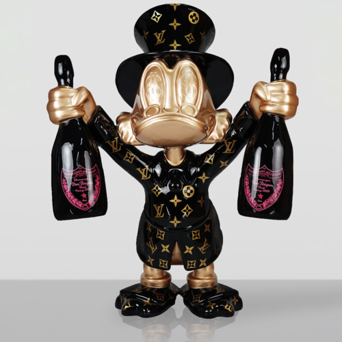 Sculpture of a duck character with golden face and hands, wearing a black outfit and top hat decorated with gold Louis Vuitton monogram patterns, holding a bottle of Dom Pérignon champagne in each hand against a plain gray background.