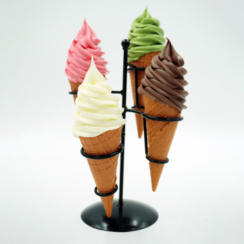 Four ice cream cones with swirled soft serve in pink, green, white, and chocolate colors, held upright by a black metal stand against a white background