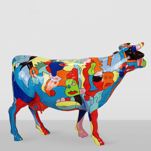 Colorful cow sculpture painted with abstract, cartoon-like faces and shapes in bright red, blue, yellow, green, and orange against a plain gray background.