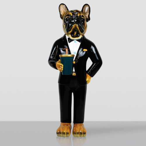 Ceramic figurine of a French bulldog standing upright, dressed in a black tuxedo with a bow tie, holding a blue cup with a brown straw, against a plain light gray background.