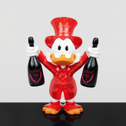 Figurine of a duck character wearing a red Louis Vuitton patterned suit and top hat, holding a bottle of Dom Pérignon champagne in each hand, standing on a reflective black surface against a plain light background.