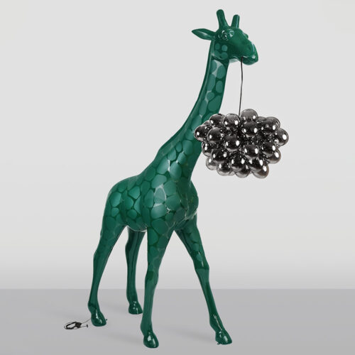 Glossy dark green giraffe sculpture holding a cluster of reflective metallic black balloons in its mouth, standing on a gray surface against a plain light gray background.