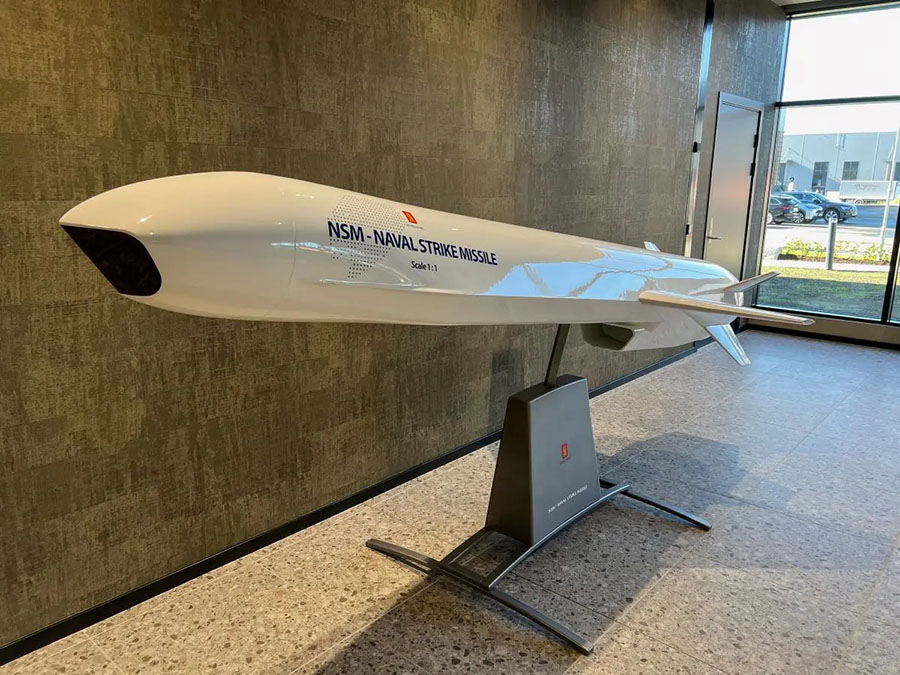 Biała figura z laminatu w skali 1:1 przedstawiająca NSM - Naval Strike Missile ustawiona na metalowym stojaku w holu.